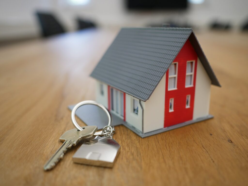 A small red and white house figurine on a table next to some house keys
