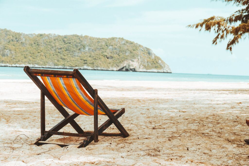 A stripy deck chair on a sandy beach near the sea.