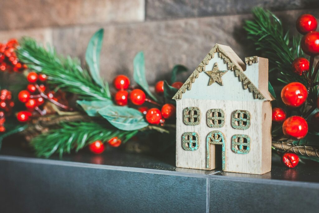 A wooden model of a house on a fireplace surrounded by winter berries and leaves