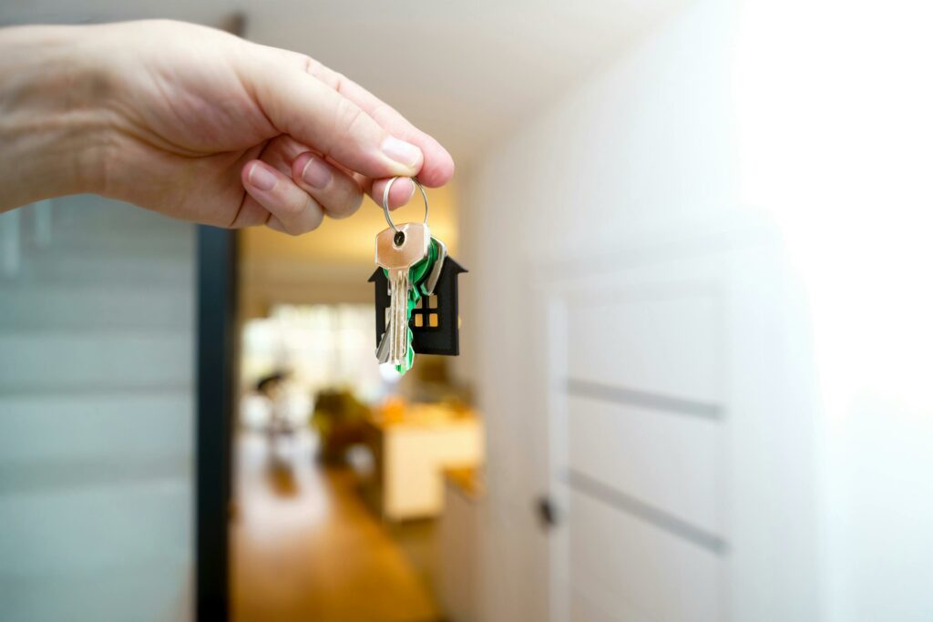 An estate agent's hand holds a set of keys with a keyring on it inside a house
